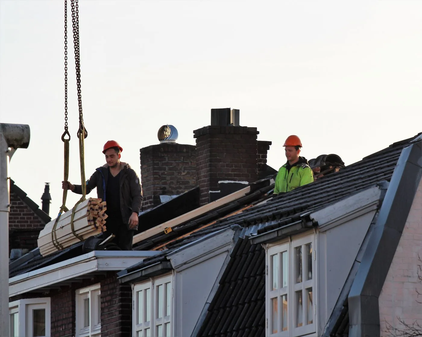 Roofing materials being lifted to workers on a roof — illustrative stock photo